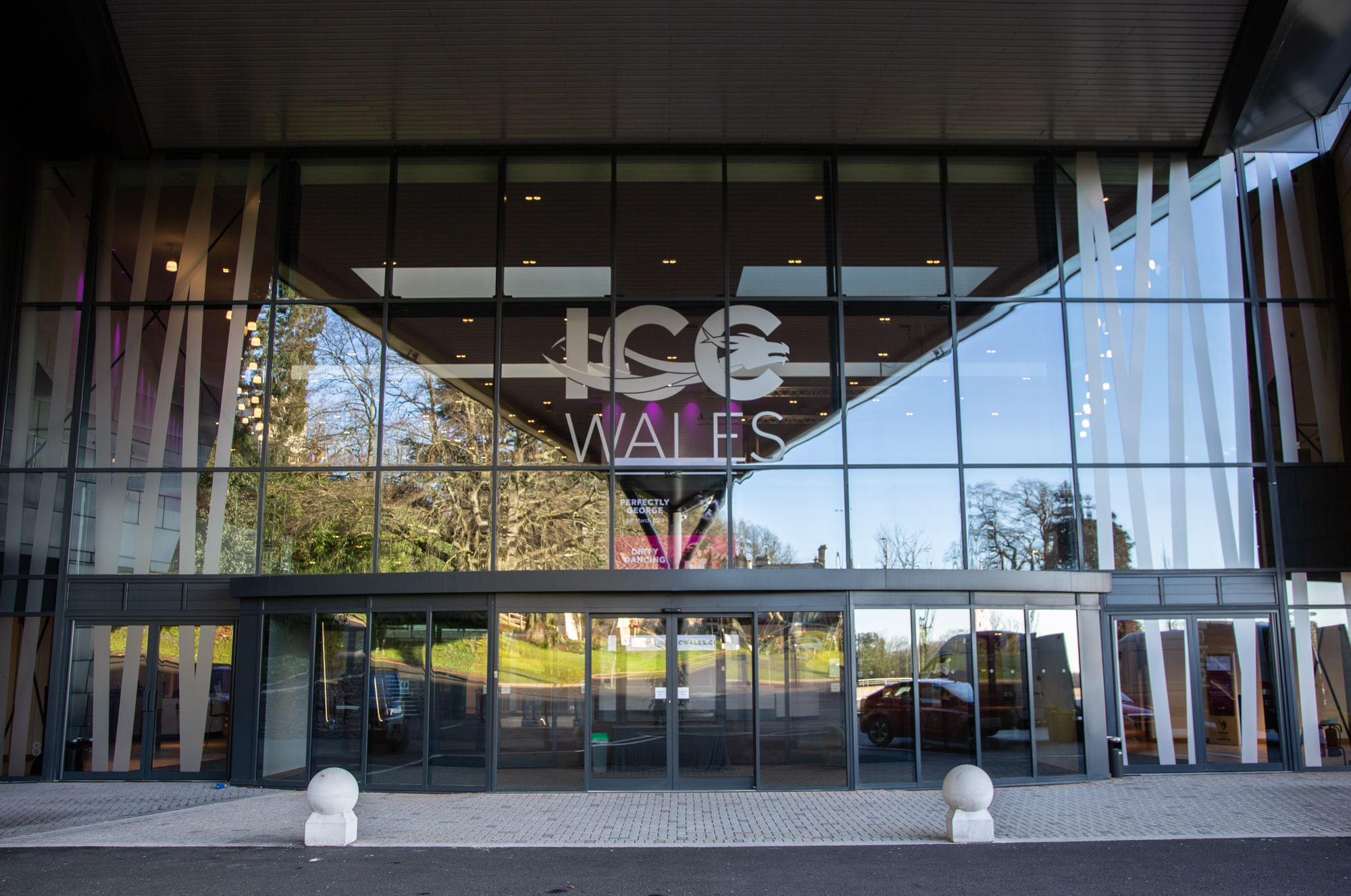 Front view of the ICCW building in Wales. It has a large glass front with the logo above the doors.