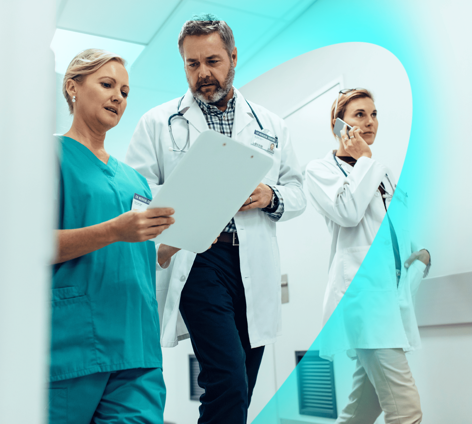 Three healthcare professionals in uniform walk along a corridor. One is talking on a mobile device while the other two look at a clipboard.