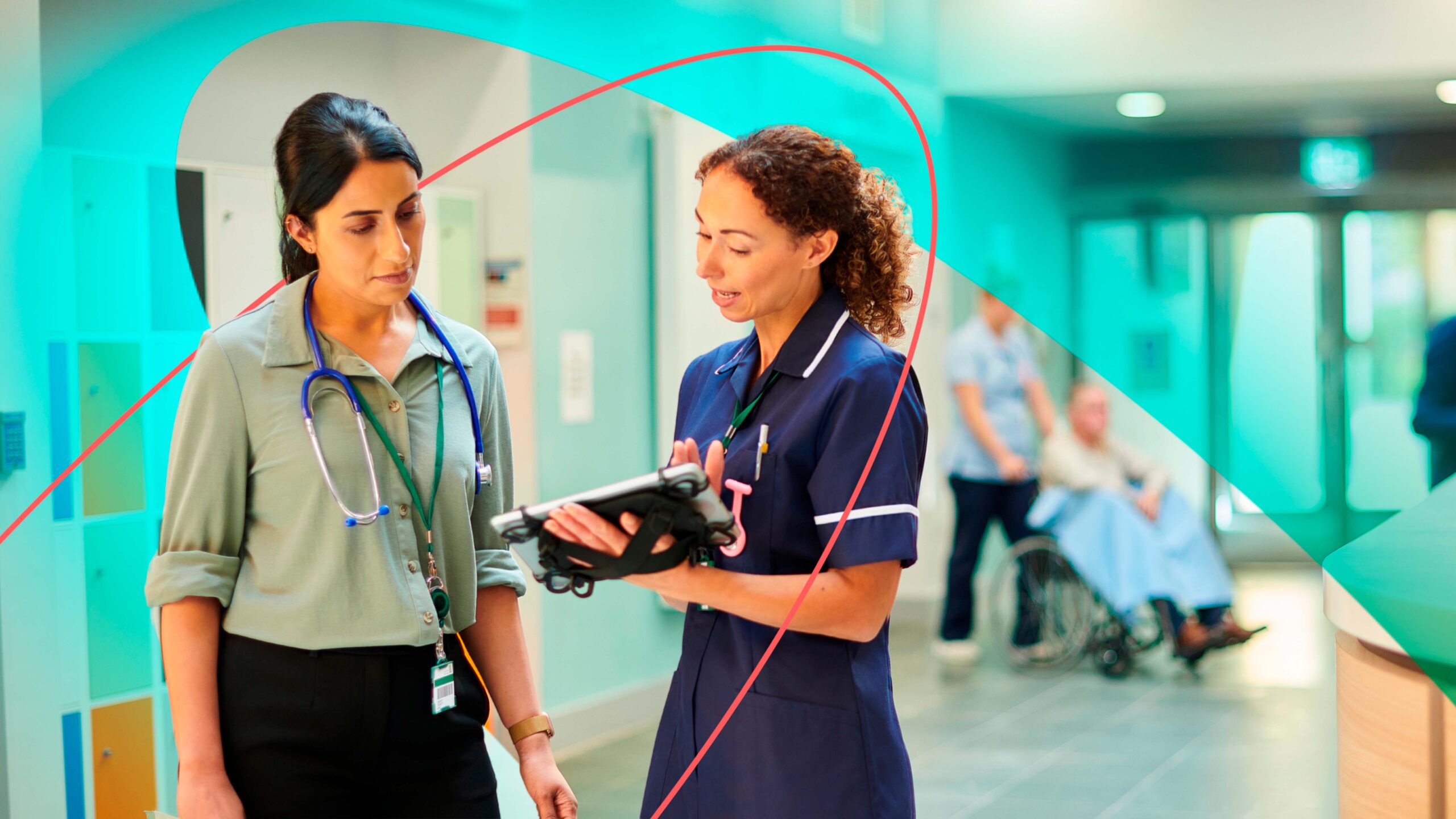 Two health professionals stand looking at a connected tablet together in a hospital